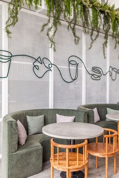 a living room filled with furniture and plants hanging from the wall above it's windows