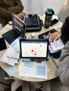 three people sitting at a table with laptops and notebooks on top of it