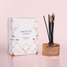 an empty box next to a candle and reeds on a pink background with gold accents