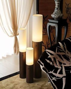 three tall candles sitting next to each other in front of a window with drapes