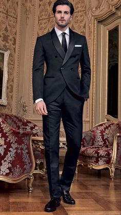 a man in a black suit and tie standing on a wooden floor next to couches