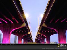 an image of a bridge that is lit up with purple lights and people walking on the sidewalk