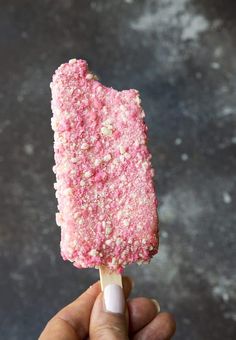 a hand holding a pink and white ice cream on a stick with sprinkles