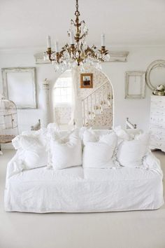 a white couch with many pillows on it and a chandelier hanging from the ceiling