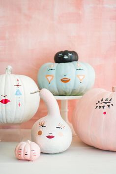 three pumpkins with faces painted on them sitting in front of a pink wall and some other decorative items