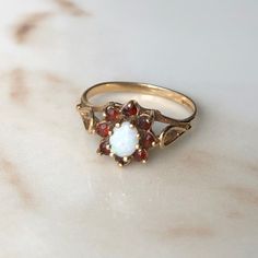 A vintage 9 carat gold Garnet and opal cluster ring. This beautiful piece holds a gorgeous collection of red stones in a gold setting, with a white opal in the centre. CONDITION: Wear consistent with age and use. Please see photos for more detail. ASSAYED IN BIRMINGHAM CIRCA.1991 SETTING: 9mm x 8mm SETTING HEIGHT: 6mm BAND WIDTH: 1.5 RING SIZE: UK: M | US: 6 1/4 WEIGHT: 1.6 grams (SZ) Vintage Multi-stone Opal Ring Gift, Vintage White Ruby Ring For Anniversary, Vintage Yellow Gold Opal Ring Birthstone, Vintage Opal Birthstone Ring Gift, Victorian Multi-stone Opal Ring As Gift, Victorian Multi-stone Opal Ring For Gift, Victorian 14k Gold Opal Ring Gift, Vintage White Cluster Ring With Gemstone, Vintage White Opal Ring For Formal Occasions