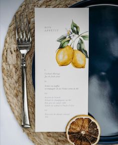 a table setting with an orange slice and silverware on it, next to a menu