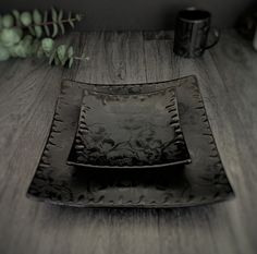 a black plate sitting on top of a wooden table next to a cup and plant