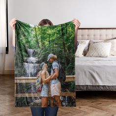 a man and woman standing in front of a bed holding up a blanket with the image of a waterfall