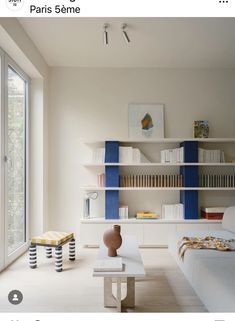 a living room filled with white furniture and bookshelves next to a large window