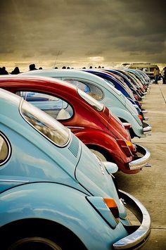 a row of cars parked next to each other on top of a parking lot in front of a cloudy sky