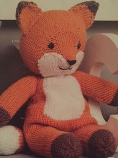 an orange knitted teddy bear sitting next to a roll of toilet paper on a shelf