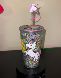 a cup with a unicorn on it sitting on top of a black table next to a lamp