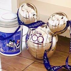 two silver mickey mouse ornaments next to a canister with a blue ribbon around it