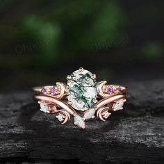 a ring with an oval shaped green stone surrounded by pink and white opal stones