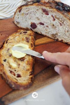 someone cutting up some bread on a wooden board with butter and raisins in it