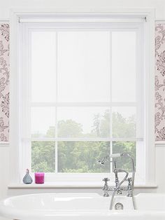 a bath tub sitting under a window next to a wallpapered wall with pink flowers