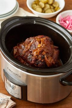 a slow cooker filled with food on top of a wooden table next to plates and utensils