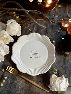 a white plate with the words happy birthday written on it next to flowers and candles