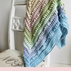 a multicolored crocheted blanket sitting on top of a white wooden chair