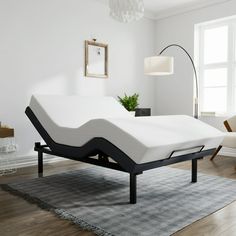 a white bed with black frame in a living room next to a chair and lamp