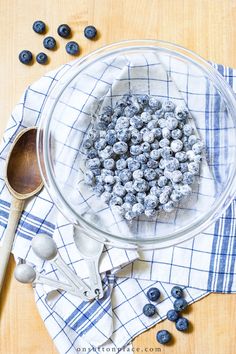 a glass bowl filled with blueberries on top of a table next to spoons