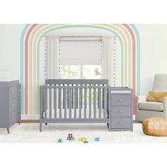 a baby's room with a crib, dresser and chair in it that has rainbow stripes on the wall