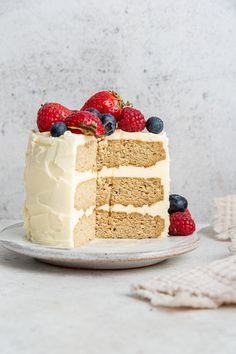 a slice of cake with white frosting and berries on top is sitting next to the rest of the cake