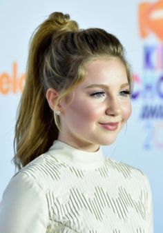 a woman with long hair wearing a white dress and smiling at the camera while standing in front of an orange carpet