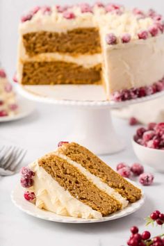 a slice of cake on a plate with cranberries around it and the rest of the cake in the background