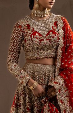 a woman in a red and gold bridal outfit with her hands on her hips