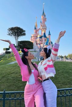 two women standing in front of a castle with their arms up and one holding her hand out