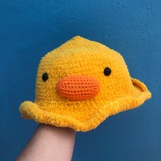 a crocheted yellow ducky hat is held by a person's hand