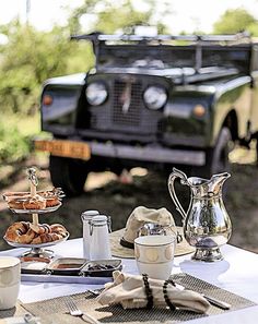 a table with plates, cups and silverware on it in front of an old car