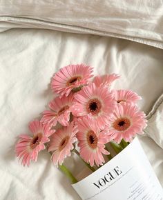 pink gerberia flowers in a vase sitting on a bed with white linens