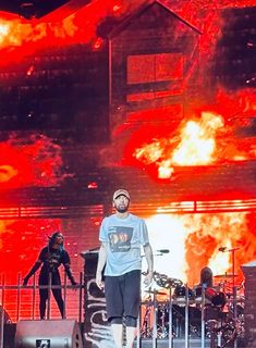 a man standing on top of a stage in front of a fire filled building with flames