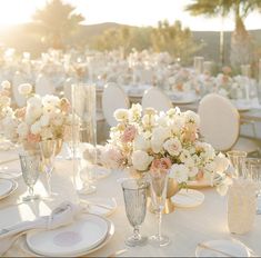 the table is set with white and pink floral centerpieces, silverware, and wine glasses