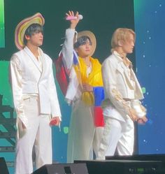 three men in white suits on stage with one holding his hand up to the sky