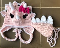 a crocheted hat with a pink and white unicorn on the front is laying on a tile floor