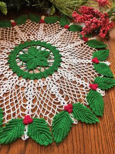 a crocheted doily with holly leaves and berries on the edge, sitting on a wooden table