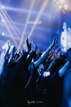 a group of people at a concert with their hands in the air and lights on