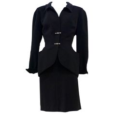 This THIERRY MUGLER skirt suit is composed of a black polyester fabric. Features a classic Mugler silhouette with nipped waist and curved bust-line to neckline design. The jacket has front snap closures, rounded shoulders, and silver and rhinestone hardware detail. The classic pencil style skirt features a zipper closure. In good vintage pre-owned condition. Made in France. Measurements in Inches: Jacket Bust: 38 Waist: 29 Skirt Waist: 26 Hip: 40 Length: 21 Classic Black Skirt Suit For Semi-formal Occasions, Elegant Fitted Black Skirt Suit, Formal Black Fitted Skirt Suit, Black Fitted Skirt Suit For Formal Occasions, Vintage Black Skirt Suit For Formal Occasions, Vintage Black Fitted Skirt Suit, Vintage Black Skirt Suit For Work, Mugler Skirt, Black Skirt Set