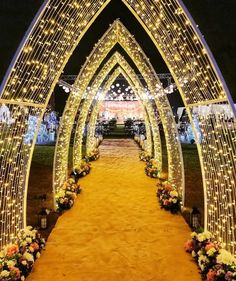 an archway decorated with lights and flowers on the side is lit up for a wedding