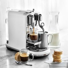 an espresso machine with two cups of coffee on the counter next to some cookies