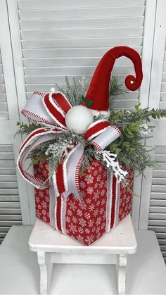 a christmas present wrapped in red and white ribbon with a santa hat on top, sitting on a stool