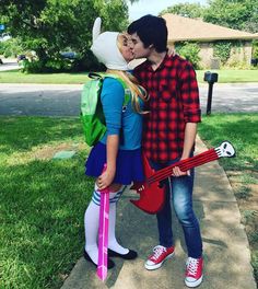 two people are kissing while standing on the sidewalk with backpacks and guitar strings in front of them