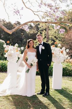 a bride and groom standing in front of their wedding arch with white flowers on it