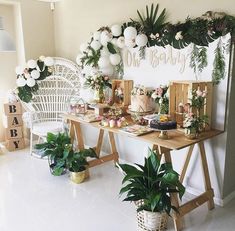 a table topped with lots of cake next to potted plants and balloons on the wall