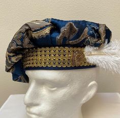 A new adult professional quality Renaissance Medieval Tudor muffin poet floppy hat. This blue and gold brocade hat is embellished with a gold trim band and a white ostrich feather.  Inside lining. New not worn. A great accent for your Medieval Renaissance outfit for your reenactment event, theme party or stage production. Sales final. Will exchange for a different size. Size X small has a 21 1/2" band Size small has a 22" band Size medium has a 22 1/2" band Size large has a 23" band Size X large Gold Costume Hats With Round Crown, Traditional Costume Hats And Headpieces For Carnival, Blue Costume Hat For Carnival, Gold Mardi Gras Costume Hats And Headpieces, High Crown Costume Hat For Mardi Gras, High Crown Costume Hats And Headpieces For Mardi Gras, Blue Carnival Costume Accessories, Mardi Gras Costume Hat With High Crown, M Hat