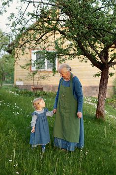 an older woman and young child standing in the grass near a tree, holding hands